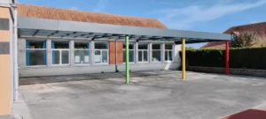 Préau aluminium MODULEO adossé avec poteaux colorés installé dans la cour maternelle de l’École du Sacré-Cœur de Baisieux par Newtech Fermetures.