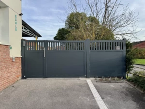 Portail aluminium sur mesure installé à l’École du Sacré-Cœur de Baisieux par Newtech Fermetures, modèle semi-ajouré RAL 7016 avec clôture assortie.