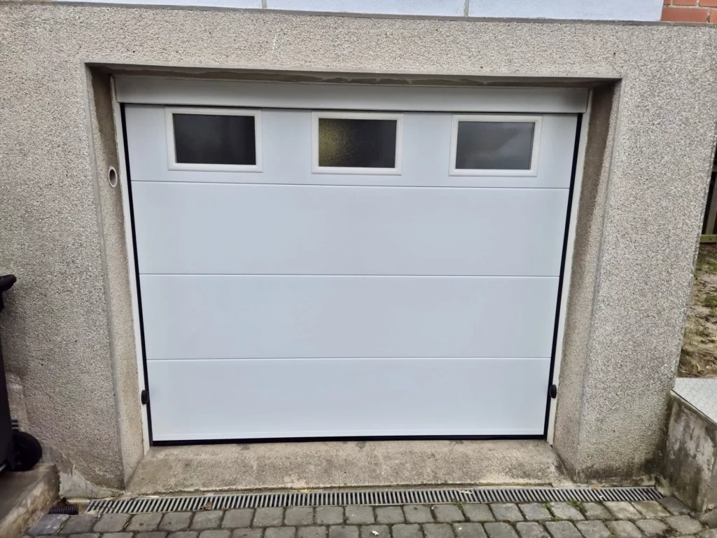 Porte de garage sectionnelle motorisée blanche avec hublots installée à Pont-à-Marcq par Newtech Fermetures
