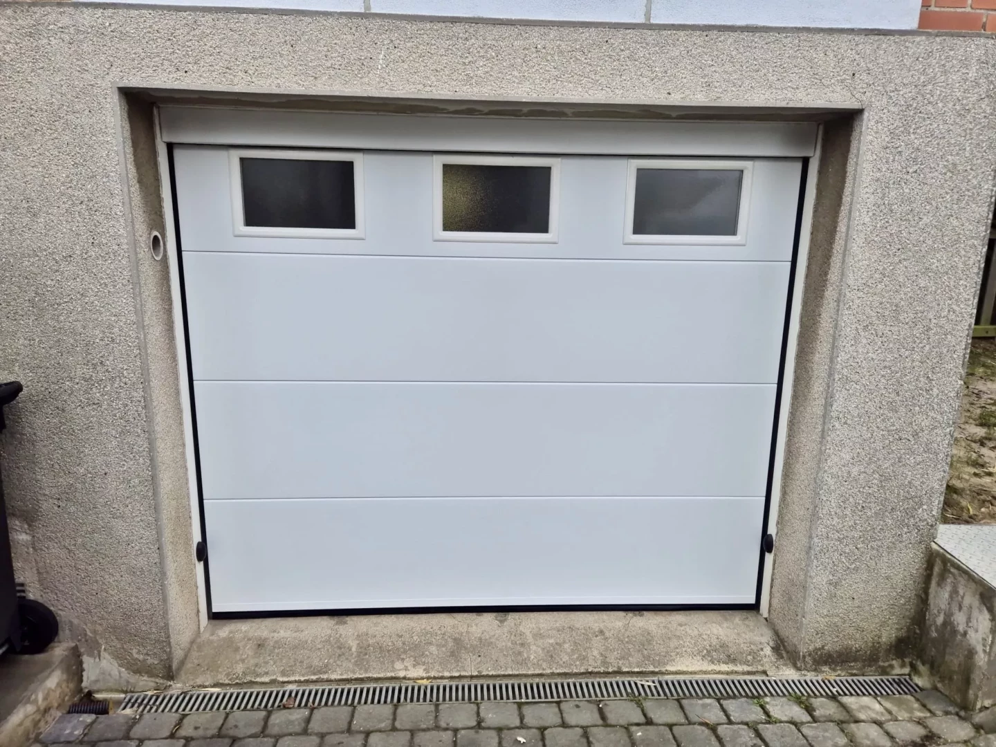 Porte de garage sectionnelle motorisée blanche avec hublots installée à Pont-à-Marcq par Newtech Fermetures