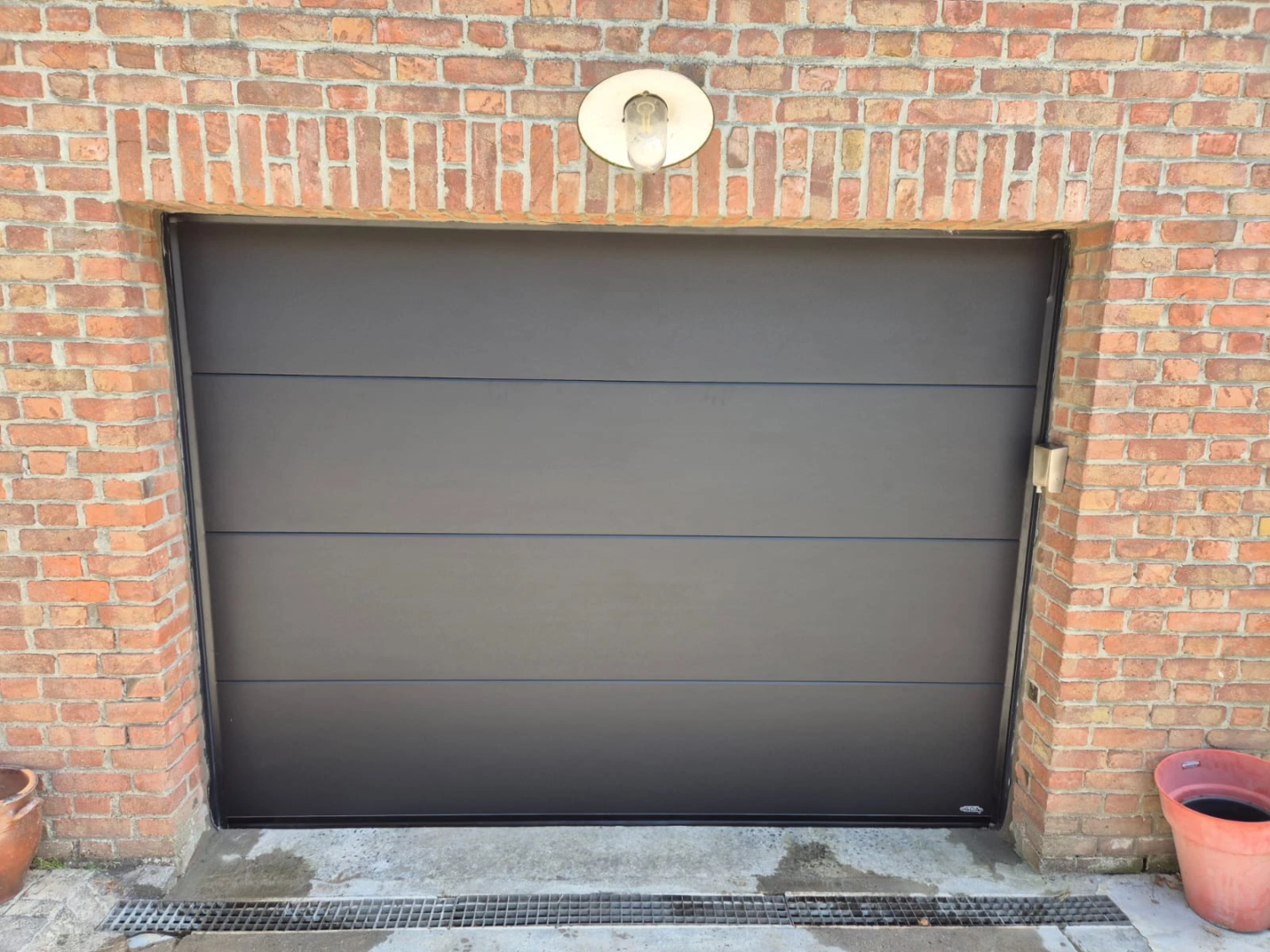 Porte de garage sectionnelle foncée installée sur une maison en briques à Genech par Newtech