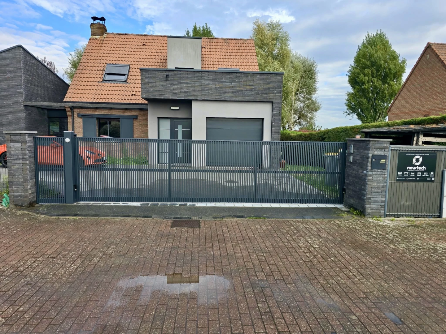 Portail coulissant Quesnoy-sur-Deûle en aluminium gris 7016, fermé, entre deux piliers en briques sombres
